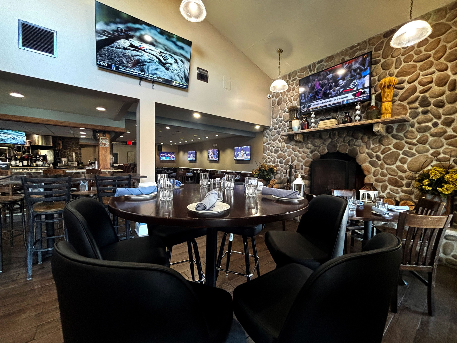 A table set beside the stone fireplace in the dining room, with TVs and the bar beyond